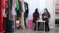 Dressmaker talking about new colletion to a customer, while drinking tea sitting on a sofa in her sewing atelier