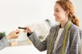 Smiling red-haired female tailor taking credit card