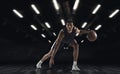 Young African sportsman, basketball player training in gym, idoors isolated on dark background. Concept of sport, game Royalty Free Stock Photo