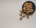 Dried almonds spilled from a dark plate onto a gray background. healthy food for raw foodists and vegetarians.