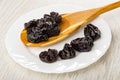 Dried black plums in spoon, few prunes in plate on wooden table