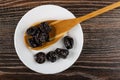 Dried black plums in spoon, prunes in white plate on wooden table. Top view