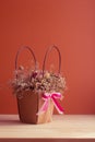 Dried bouquet of flowers in a pink tinted paper basket with a bow on a orange background