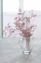 Dried bouquet of violet pink flowers in transparent glass vase on at the light gray table in the white interior vertical Royalty Free Stock Photo