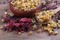 Dried chamomile flowers in a wooden spoon, blended tea in a bowl, hibiscus and thyme on a wooden table. traditional medicinal herb