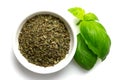 Dried chopped basil in white ceramic bowl next to fresh basil leaves isolated on white from above