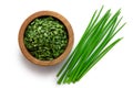 Dried chopped chives in a dark wood bowl next to a pile of whole fresh chives isolated on white from above