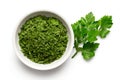 Dried chopped parsley in white ceramic bowl next to fresh parsley leaves isolated on white from above