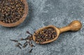 Dried cloves in wooden shovel and bowl on grey rustic table