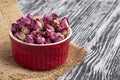 Dried damask rose buds in small r.ed bowl on black wooden table