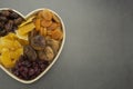 Dried fruits mix, in wooden heart shape box isolated on dark background. Top view of various dried fruits figs, apricots, mango,