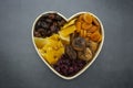Dried fruits mix, in wooden heart shape box isolated on dark background. Top view of various dried fruits figs, apricots, mango,