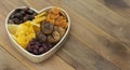 Dried fruits mix baner in wooden heart shape box isolated on wooden background. Top view of various dried fruits figs, apricots,