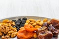 Dried fruits and nuts lie on a silver tray on a white wooden background