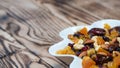 Dried fruits in white plate on wooden table, copy space for text. Mix of different varieties of nuts and berries, vitamins Royalty Free Stock Photo