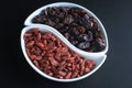 Dried goji berries and raisins into a bowl on a dark background, like a yin-yang