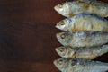 Dried herrings lined up in a row against a wooden backgournd.