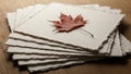 A dried maple leaf lies on top of a stack of textured, deckle-edged paper sheets Royalty Free Stock Photo