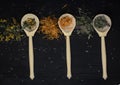 dried medicinal herbs in wooden spoons and scattered on a black wooden background