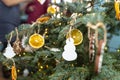 Dried orange slices and a white snowman hanging on a Christmas tree, with Christmas lights and people in the background. Royalty Free Stock Photo