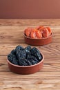 Dried prunes and dried apricots lying in ceramic bowls on a wooden table. Closeup