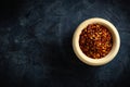 Dried red pepper flakes in a wooden bowl. Chili pepper flakes on a dark background.