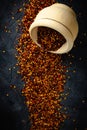 Dried red pepper flakes in a wooden bowl. Chili pepper flakes on a dark background. Top view