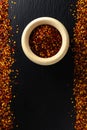 Dried red pepper flakes in a wooden bowl. Chili pepper flakes on a dark background. Top view