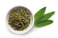 Dried rubbed sage in a white ceramic bowl next to fresh sage leaves isolated on white from above