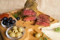 Dried tenderloin of beef meat, thinly sliced, on the wooden serving board with cheese, olives, black pepper, tomato