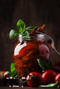 Dried tomatoes in olive oil with green basil and spices in glass jar on wooden kitchen table, rustic style, place for text Royalty Free Stock Photo