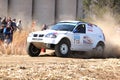 Drifting white BMW rally car kicking up dust on turn.