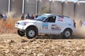 Drifting white BMW rally car kicking up dust on turn.