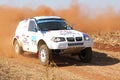 Drifting white BMW rally car kicking up dust on turn.