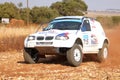 Drifting white BMW rally car kicking up dust on turn.