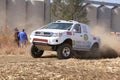 Drifting white Toyota truck kicking up dust on turn ar rally.