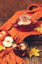 Drink autumn apple red berries in a glass teapot and an orange scarf on a wooden background. Hot fruit berry tea.