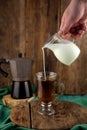 Milk is poured into decanter coffee. Geyser coffee maker, creamer on a wooden table. Glass cup with coffee making cappuccino.