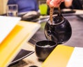 Drink Hot Tasty Herbal Matcha Green Tea in black earthenware cup, serving from kettle in restaurant background. Having healthy Royalty Free Stock Photo