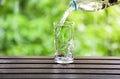 Drink water pouring into glass on wooden table with natural lighting and background in daylight Royalty Free Stock Photo