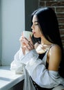 Drink well feel well. Pretty woman drinking healthy morning drink at window. Adorable girl holding cup with tasty coffee