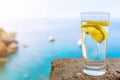 Drinking glass with cold carbonated water or soft drink and lemon slice against blue sea and sky Royalty Free Stock Photo