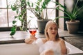 Drinking red wine beautiful blonde young woman taking bath with bubbles in bathroom interior