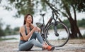 Drinking water. Female cyclist with good body shape sitting near her bike on beach at daytime Royalty Free Stock Photo