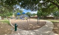 Drinking water fountain in public community park playground structure wood chips mulch, concrete sidewalk pathway, metal fence