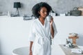 Drinks from cup. Young african american woman with curly hair indoors at home