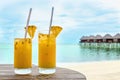 Drinks with a straw on a wooden table on the background of a sandy beach and houses on the water Royalty Free Stock Photo
