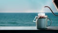 Dripping Coffee by the Sea Side at Morning. Making Hot Drink by Pouring Hot Water from kettle into an Instant Coffee Drip Bag at Royalty Free Stock Photo