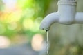 Dripping faucet in white close-up against the background of a green garden. Royalty Free Stock Photo