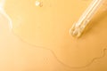 Dripping hydrophilic oil from pipette on beige background, top view